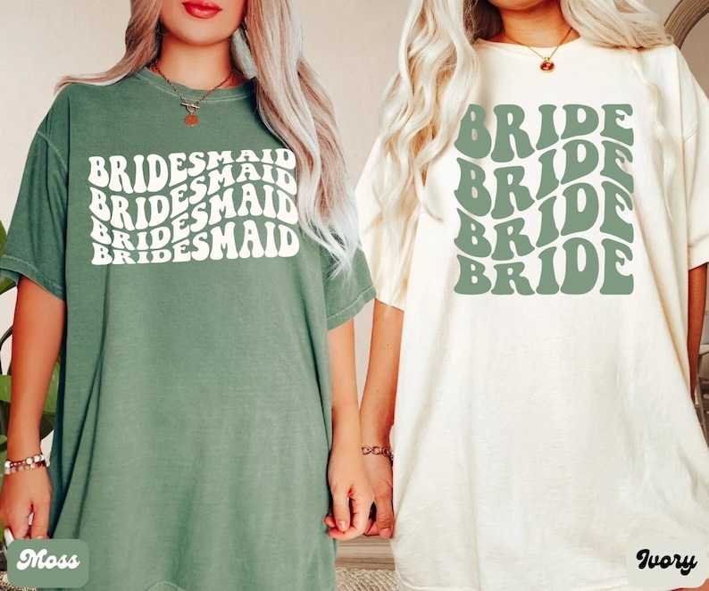 May include: Two t-shirts with a retro design. One is green with the word "BRIDESMAID" repeated in white. The other is ivory with the word "BRIDE" repeated in green.