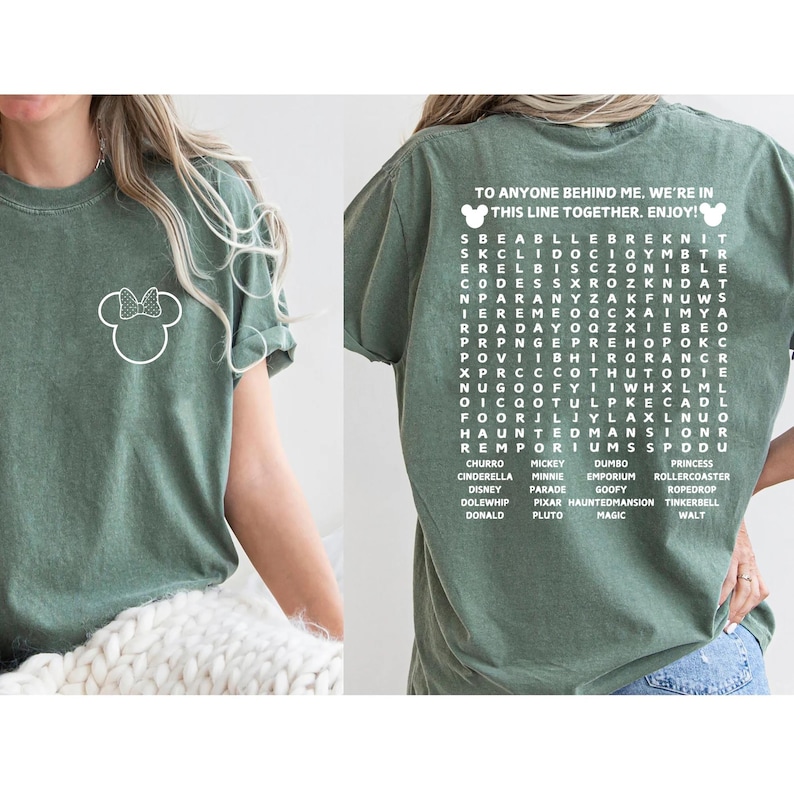 Puede incluir: Camiseta verde oliva con un contorno blanco de Minnie Mouse en la parte delantera. La parte trasera de la camiseta tiene el texto "TO ANYONE BEHIND ME, WE'RE IN THIS LINE TOGETHER. ENJOY!" y un juego de b&uacute;squeda de palabras de Disney.