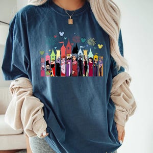 Puede incluir: Camiseta azul marino con un gr&aacute;fico colorido de villanos de Disney frente a un castillo, con fuegos artificiales y siluetas de Mickey Mouse. La palabra "midnight" est&aacute; impresa en oro en la parte inferior.