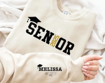 May include: A white sweatshirt with black text that says "Senior 2025" and a black graduation cap. The sweatshirt also has a smaller black graduation cap and the text "Melissa" in gold.