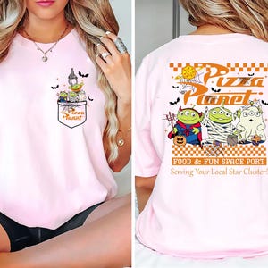 Pode incluir: Camiseta rosa claro com design Pizza Planet. O gr&aacute;fico do bolso frontal inclui alien&iacute;genas e morcegos. A parte de tr&aacute;s exibe o logotipo Pizza Planet e alien&iacute;genas com tema de Halloween. Um estilo divertido e casual.