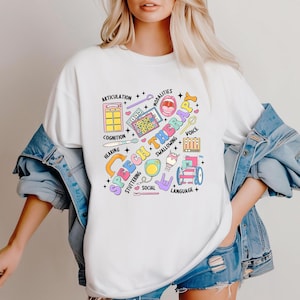 May include: White t-shirt with a colorful graphic design that says "Speech Therapy" and includes illustrations of various speech therapy tools and concepts, such as a microphone, a tongue depressor, and a speech bubble.