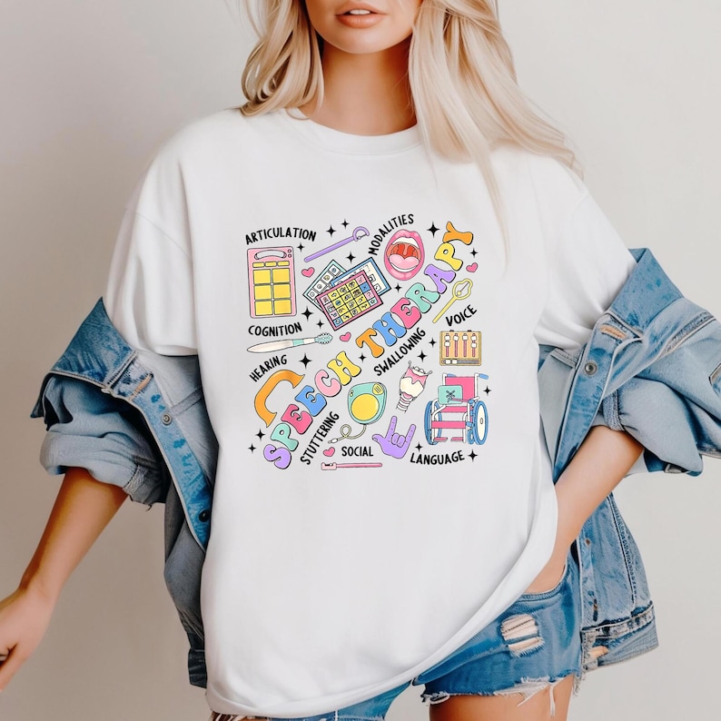 May include: White t-shirt with a colorful graphic design that says "Speech Therapy" and includes illustrations of various speech therapy tools and concepts, such as a microphone, a tongue depressor, and a speech bubble.
