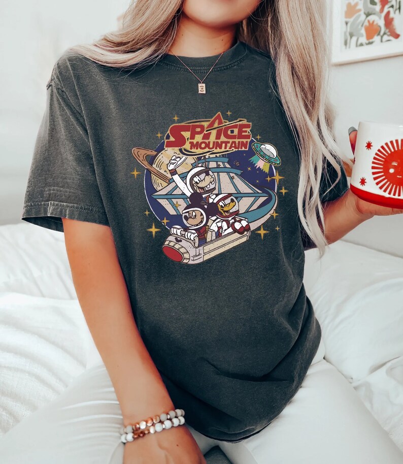 May include: A dark gray t-shirt with a vintage-style graphic of Mickey Mouse and Donald Duck riding a spaceship in space. The graphic includes the text "Space Mountain".