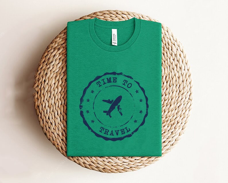 Puede incluir: Una camiseta verde con un dise&ntilde;o de sello azul que dice "Time to Travel" con un avi&oacute;n y una tabla de surf.