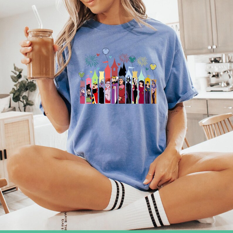 Puede incluir: Camiseta azul claro con un gr&aacute;fico colorido de villanos de Disney frente a torres de castillos. El gr&aacute;fico incluye fuegos artificiales y globos. La camiseta est&aacute; hecha de un material suave.