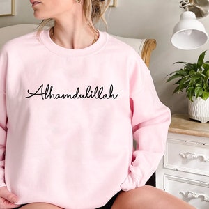 May include: A pink sweatshirt with the phrase "Alhamdulillah" written in black cursive.