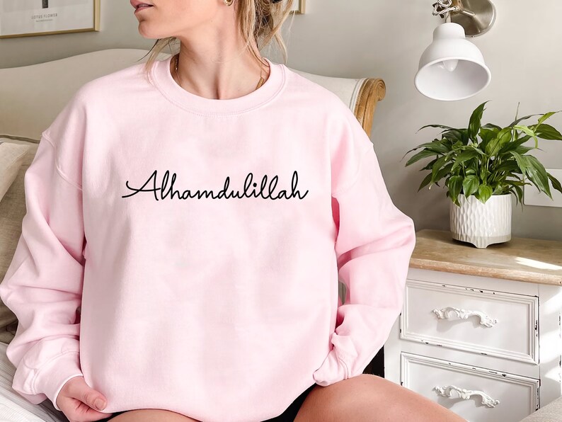 May include: A pink sweatshirt with the phrase "Alhamdulillah" written in black cursive.