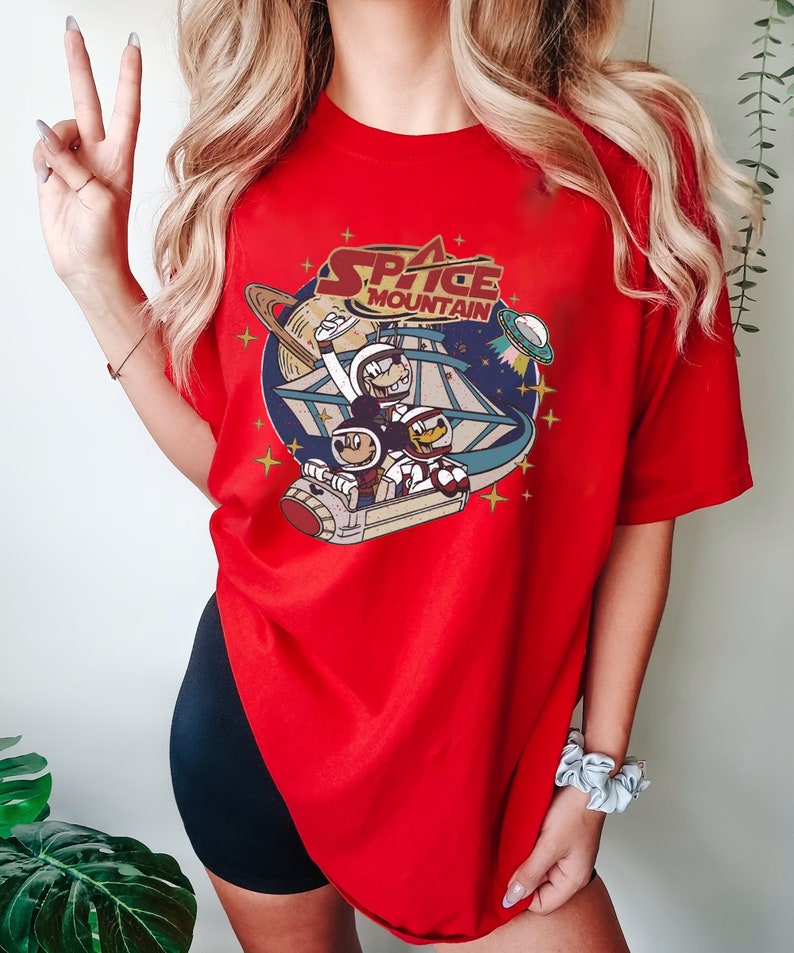 May include: Red t-shirt with a graphic of Mickey Mouse and friends riding a rocket in space. The text "Space Mountain" is printed on the shirt.