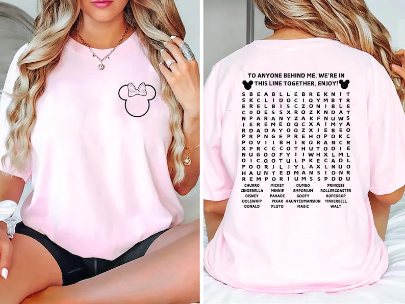 Puede incluir: Camiseta rosa claro con un contorno negro de Minnie Mouse y un lazo en la parte delantera. La parte trasera presenta una b&uacute;squeda de palabras con tem&aacute;tica de Disney y el texto "TO ANYONE BEHIND ME, WE'RE IN THIS LINE TOGETHER. ENJOY!"