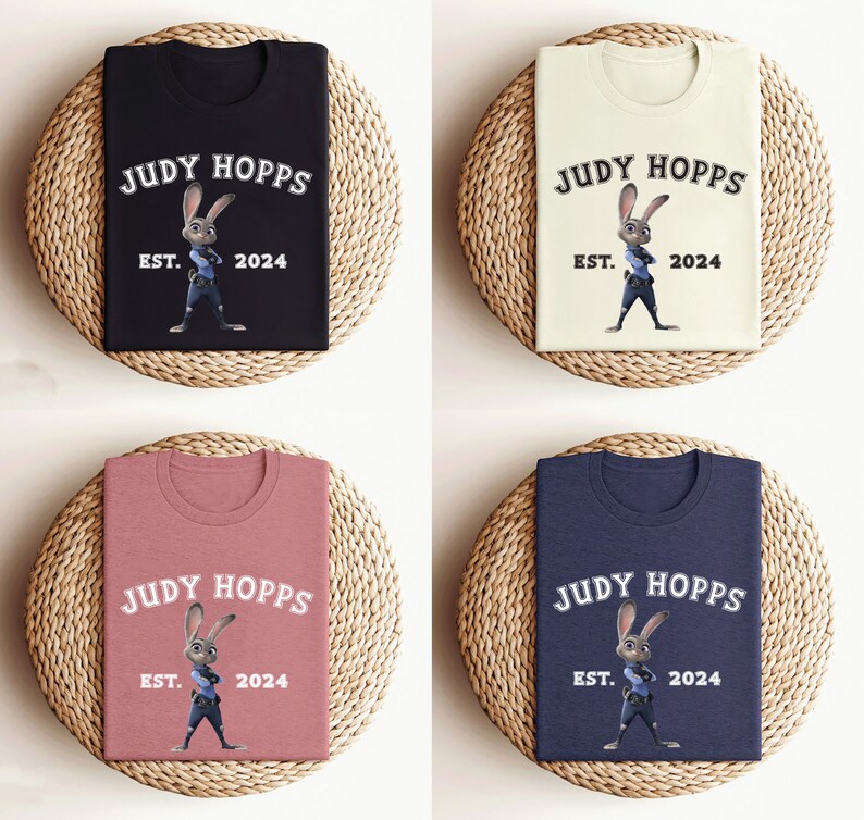 May include: Four t-shirts with different colors, black, beige, pink, and navy blue, featuring a cartoon image of Judy Hopps from the movie Zootopia. The text on the shirts reads "Judy Hopps" with "Est. 2024" underneath.