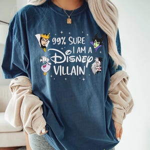 以下が含まれることがあります： 「99% Sure I am a Disney Villain」の文字とディズニーヴィランズのイラストがプリントされたネイビーブルーのTシャツ。Tシャツは濃い青色で、ゆったりとしたフィット感です。