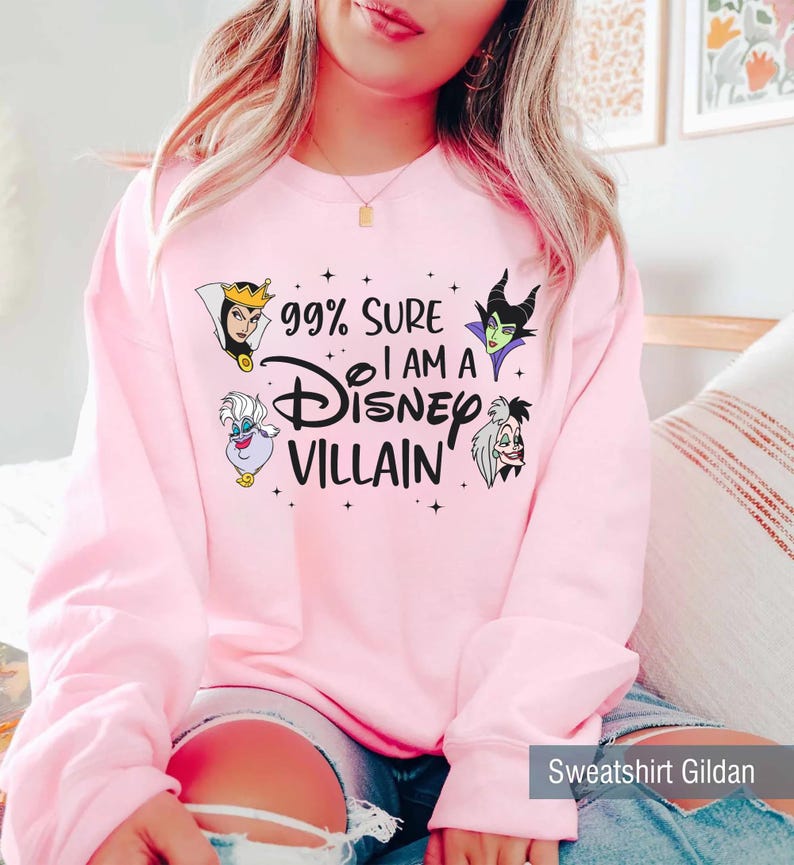 以下が含まれることがあります： 「99% Sure I am a Disney Villain」の文字とディズニーヴィランのイラストが描かれたピンク色のスウェットシャツ。Gildanブランドです。