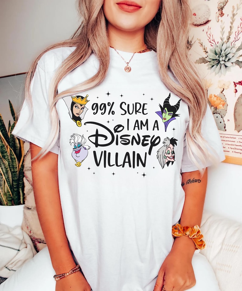 以下が含まれることがあります： 「99% Sure I Am A Disney Villain」の黒い文字が入った白いTシャツ。邪悪な女王、マレフィセント、アースラ、クルエラ・ド・ヴィルなど、ディズニーの悪役のイラストが描かれています。