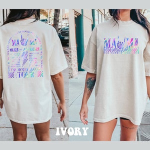 May include: A white oversized t-shirt with a holographic graphic on the front that says "MAMA" with a sign language hand symbol for "I love you". The back of the shirt has a holographic graphic that says "MAMA MAKES IT ALL HAPPEN" with a sign language hand symbol for "I love you" and the text "THE MOTHERLODE TOUR".