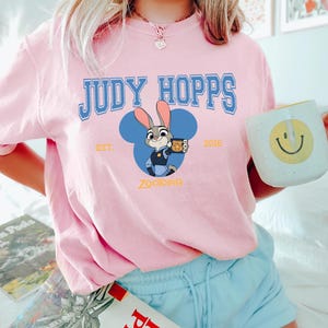 Op de afbeelding: Een witte keramische mok met een zwart handvat en de tekst "But First, Coffee" in een zwarte, vette letter. De mok staat op een houten oppervlak. De mok is ongeveer 10 cm hoog.