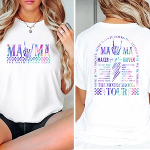 May include: White t-shirt with a rainbow graphic of the word "MAMA" with a peace sign hand gesture. The text "The Motherhood Tour" is below the graphic. The back of the shirt has a rainbow graphic of the word "MAMA" with a peace sign hand gesture and the text "Some days it rocks me either way we're rockin' makes it all happen The Motherhood Tour".