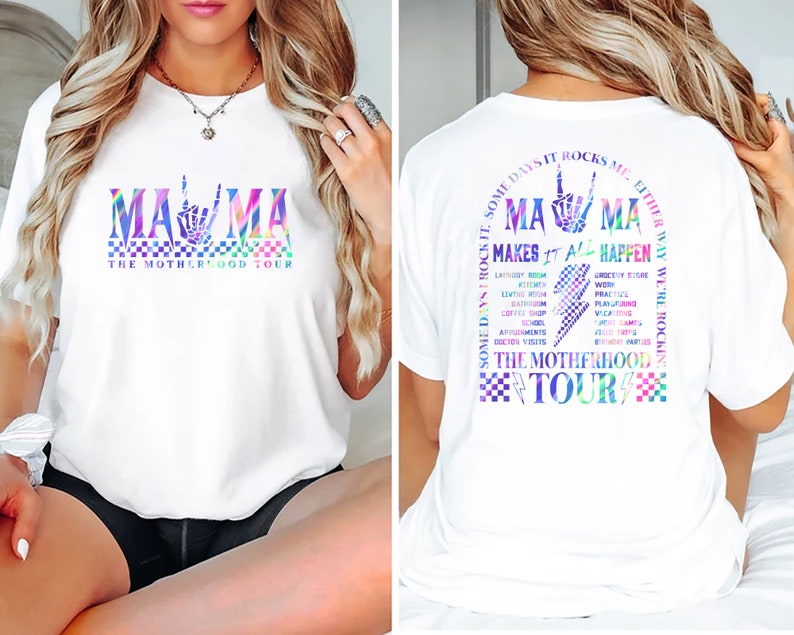 May include: White t-shirt with a rainbow graphic of the word "MAMA" with a peace sign hand gesture. The text "The Motherhood Tour" is below the graphic. The back of the shirt has a rainbow graphic of the word "MAMA" with a peace sign hand gesture and the text "Some days it rocks me either way we're rockin' makes it all happen The Motherhood Tour".