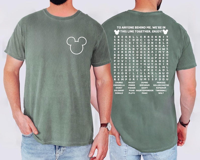 May include: Sage green t-shirt featuring a white Mickey Mouse outline on the front. The back of the shirt has a word search puzzle with the text "TO ANYONE BEHIND ME. WE'RE IN THIS LINE TOGETHER. ENJOY!" and Disney-related words.