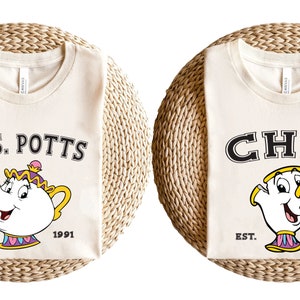 May include: Two cream colored t-shirts with a cartoon image of Chip and Mrs. Potts from Beauty and the Beast. The text on the shirts reads "Mrs. Potts" and "Chip" with the year "1991" and "EST." printed below the images.