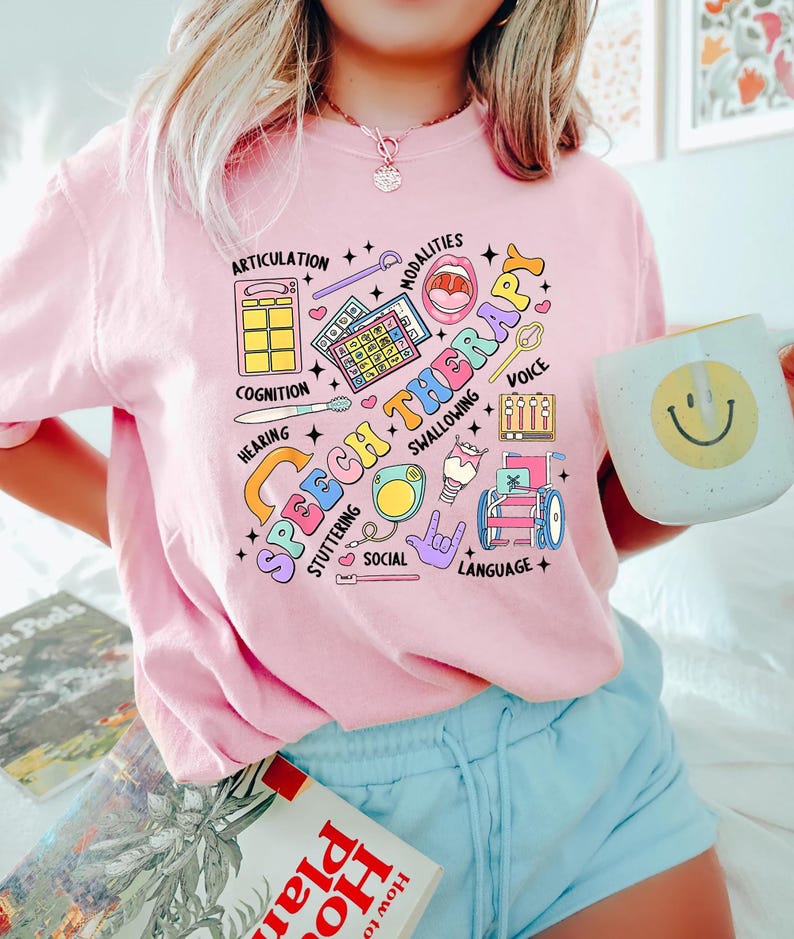 May include: Pink t-shirt with a colorful graphic design that says "Speech Therapy" and includes illustrations of various speech therapy tools and symbols.