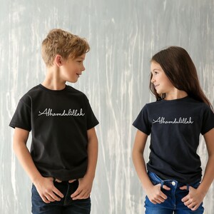 May include: Two children wearing black t-shirts with the text "Alhamdulillah" in white. The boy is wearing blue jeans and the girl is wearing blue jeans.