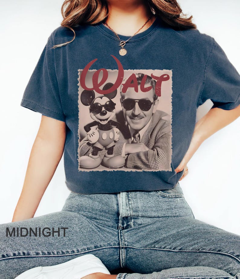 May include: A dark blue short-sleeve t-shirt featuring a graphic print of Walt Disney and Mickey Mouse both wearing sunglasses. The word Walt is printed in large red letters above the figures. The shirt has a crew neckline and a relaxed fit.