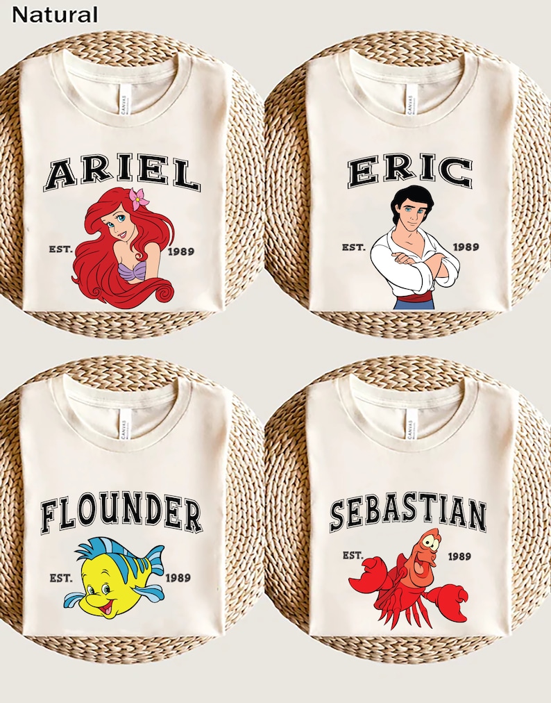 May include: Four white t-shirts with different Disney characters printed on them. The shirts feature Ariel, Eric, Flounder, and Sebastian from The Little Mermaid. Each shirt has the character's name printed in black with the text "EST. 1989" underneath.