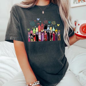 Puede incluir: Camiseta gris oscuro con un gr&aacute;fico colorido de villanos de dibujos animados frente a un horizonte de castillo. El gr&aacute;fico incluye fuegos artificiales y siluetas de Mickey Mouse. La camiseta tiene mangas cortas y un corte holgado.