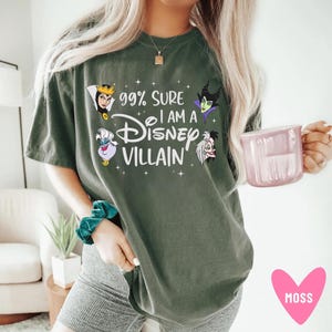 以下が含まれることがあります： 「99% Sure I am a Disney Villain」の文字とディズニーヴィランズのイラストがプリントされたオリーブグリーンのTシャツ。デザインには、邪悪な女王、アースラ、マレフィセント、クルエラ・ド・ヴィルが含まれています。ゆったりとしたフィット感のTシャツです。