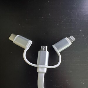 Könnte beinhalten: Ein weißes Drei-in-Eins-Ladekabel mit einem USB-C-, Micro-USB- und Lightning-Anschluss.