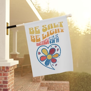 Könnte beinhalten: Eine weiße Flagge mit einem bunten Retro-Design, auf dem "Be Salt Be Light Matthew 5:13-15" steht. Das Design enthält ein Herz mit einer Blume darin.