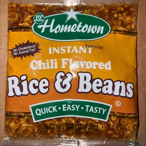 May include: A sealed package of Hometown Instant Chili Flavored Rice & Beans. The package is primarily orange with green and white text and logos. The text includes "Quick, Easy, Tasty" and "Net Wt 4.4 oz (125g)".