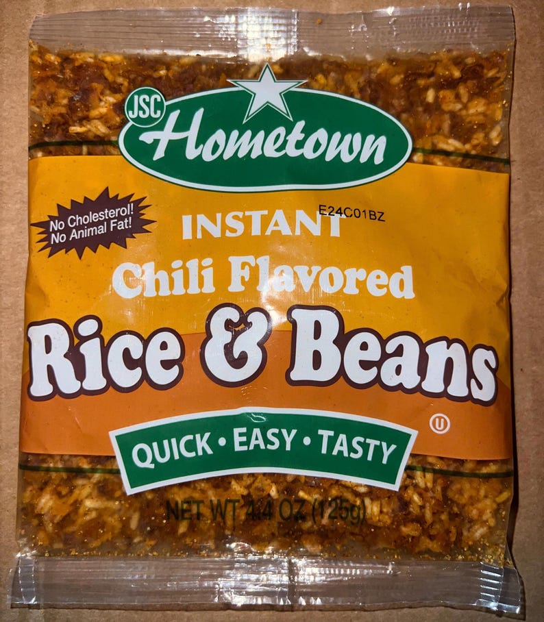 May include: A sealed package of Hometown Instant Chili Flavored Rice & Beans. The package is primarily orange with green and white text and logos. The text includes "Quick, Easy, Tasty" and "Net Wt 4.4 oz (125g)".