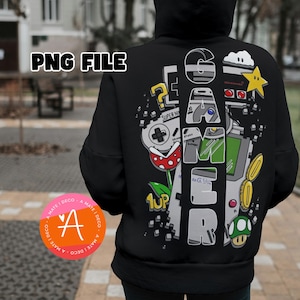 May include: Black hoodie with a large graphic on the back featuring the word "GAMER" in a stylized font, along with various video game-themed illustrations. The design includes a controller, a mushroom, and a star. The text "PNG FILE" is at the top.