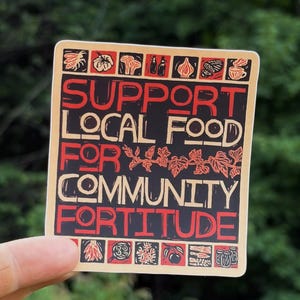 May include: A square sticker with a black background and cream border featuring the text SUPPORT LOCAL FOOD FOR COMMUNITY FORTITUDE in red and cream. The design includes small red and black illustrations of produce, jars, and plants.