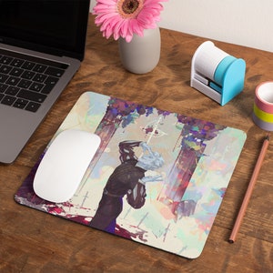 May include: A computer mouse and mouse mat on a wooden desk. The mouse mat features an artistic illustration of a figure holding a cross. A laptop, pencil, tape dispenser, and a small vase with a pink flower are also on the desk.
