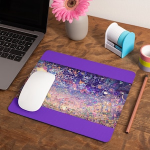 Puede incluir: Una alfombrilla de rat&oacute;n de color morado con un dise&ntilde;o abstracto colorido. La alfombrilla de rat&oacute;n tiene un borde morado y un rat&oacute;n blanco est&aacute; encima.