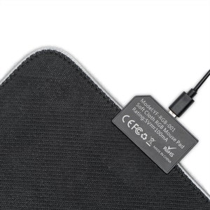 May include: Black rectangular mouse mat with a stitched edge. A black rectangular component with text is attached, and a black USB cable is plugged in. The text on the component reads "Model: YF-RGB-001 Soft Cloth RGB Mouse Pad Rating: 5V==100mA MADE IN CHINA".