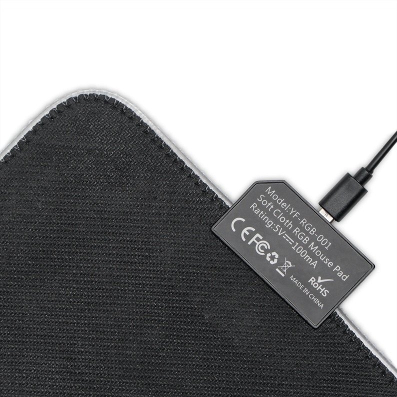 May include: Black rectangular mouse mat with a stitched edge. A black rectangular component with text is attached, and a black USB cable is plugged in. The text on the component reads "Model: YF-RGB-001 Soft Cloth RGB Mouse Pad Rating: 5V==100mA MADE IN CHINA".
