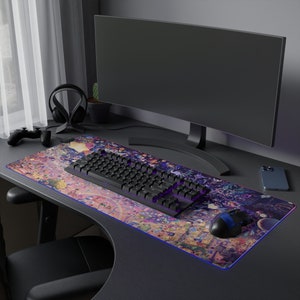 Puede incluir: Un teclado de ordenador negro con retroiluminaci&oacute;n morada se encuentra sobre una alfombrilla de rat&oacute;n colorida con un dise&ntilde;o de dibujos animados. Tambi&eacute;n se puede ver un monitor de ordenador negro y un rat&oacute;n inal&aacute;mbrico negro en el escritorio.