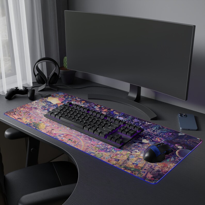 Puede incluir: Un teclado de ordenador negro con retroiluminaci&oacute;n morada se encuentra sobre una alfombrilla de rat&oacute;n colorida con un dise&ntilde;o de dibujos animados. Tambi&eacute;n se puede ver un monitor de ordenador negro y un rat&oacute;n inal&aacute;mbrico negro en el escritorio.