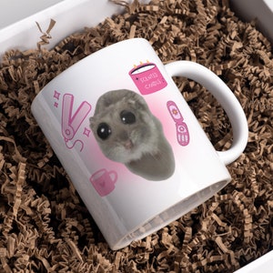 Può includere: Tazza in ceramica bianca con sfondo rosa e un'immagine di un lemure con occhi grandi in stile cartone animato. La tazza ha testo rosa che dice "Scented Candle" e altre immagini di cartoni animati rosa di una piastra per capelli, un telefono e una tazza di caffè.