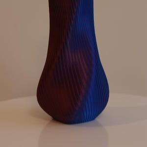 Può includere: Un vaso in ceramica blu e bordeaux con un design ondulato e nervato.