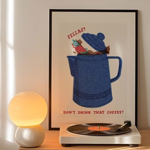 May include: A vintage-style record player with a turntable and a record on it. A lamp with a white globe sits on a wooden shelf with a record collection. A framed poster with a blue teapot and the text "FELLAS! DON'T DRINK THAT COFFEE!" is on the wall above the shelf. A framed poster with a red curtain and two figures in black and white is on the wall above the record player.