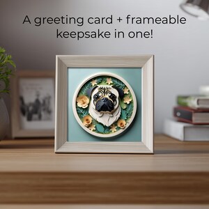 May include: A framed square art piece featuring a pug's face in a circular design. The pug is black and tan, surrounded by floral and leaf accents. The frame is light-colored, and the background is a soft teal. Text above the frame reads: "A greeting card + frameable keepsake in one!"