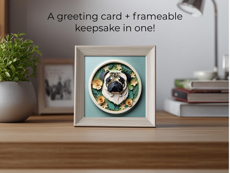 May include: A framed square art piece featuring a pug's face in a circular design. The pug is black and tan, surrounded by floral and leaf accents. The frame is light-colored, and the background is a soft teal. Text above the frame reads: "A greeting card + frameable keepsake in one!"