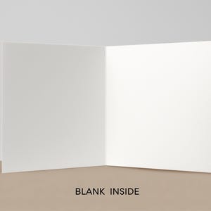 May include: An open, blank greeting card with a white interior. The card is displayed on a tan surface against a neutral background. The words "BLANK INSIDE" are printed at the bottom of the card.