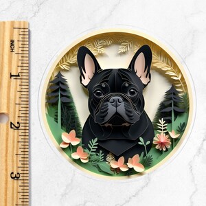 Puede incluir: Un bulldog franc&eacute;s negro con orejas marrones se representa en una obra de arte de estilo recortado en papel. El perro est&aacute; rodeado de hojas verdes y flores rosas.