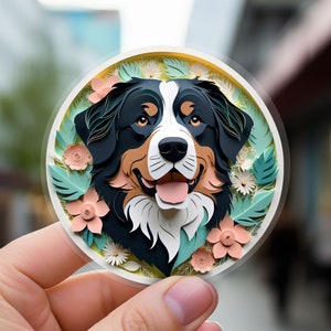 May include: A paper cut-out of a Bernese Mountain Dog's head with a floral background. The dog is smiling with its tongue out. The flowers are in shades of pink, white, and green.